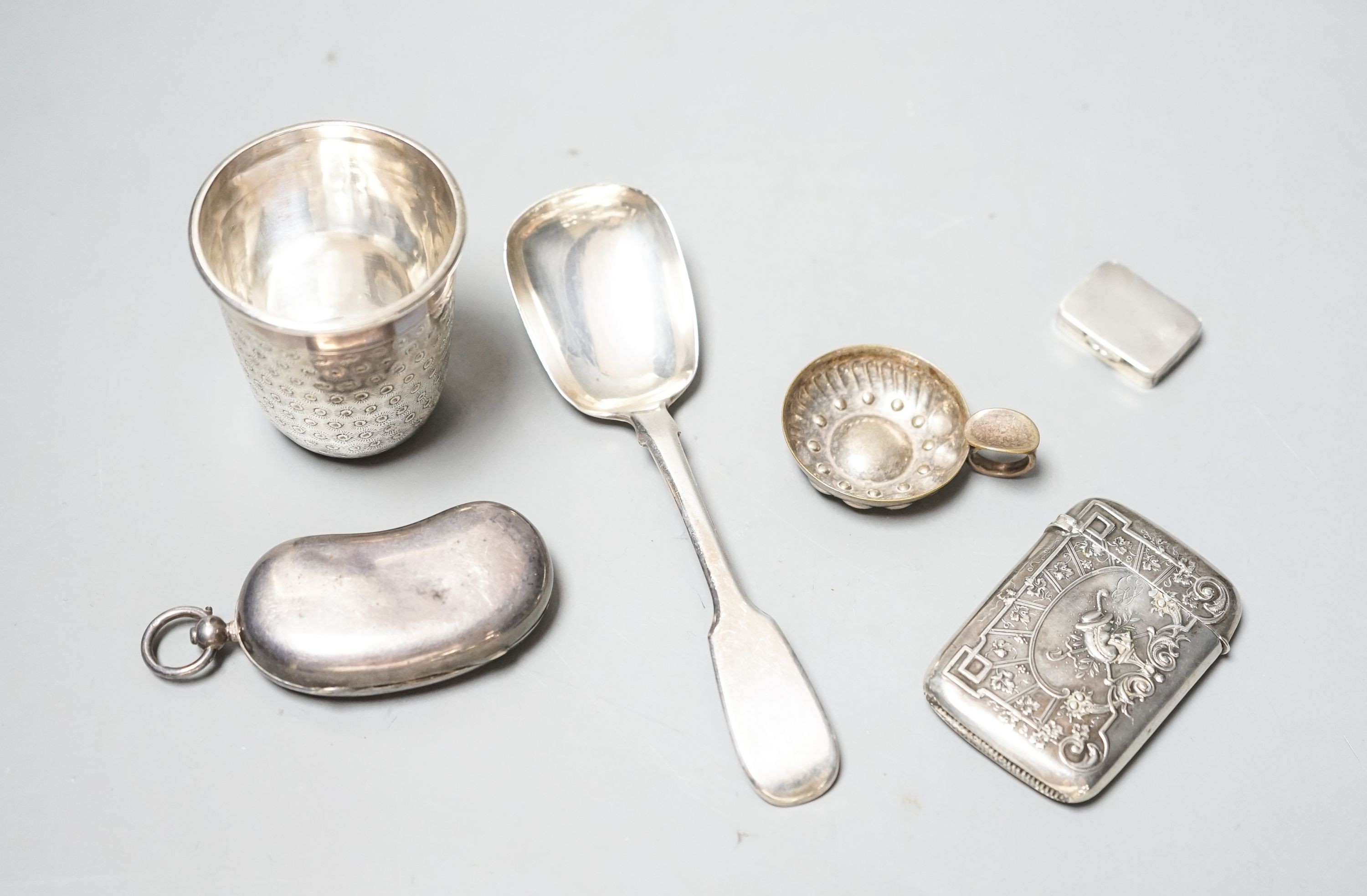 A George V silver twin sovereign kidney shaped case, 65mm, a silver spoon, silver tot , silver pill box, a German 800 vesta case and a plated small taste vin.